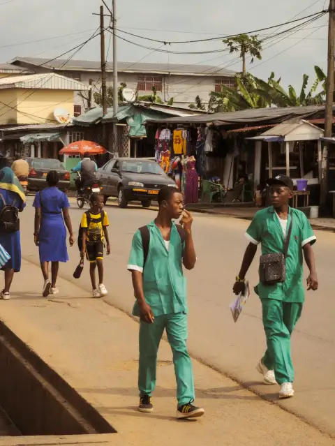 Two health workers in green scrubs walking along a busy street