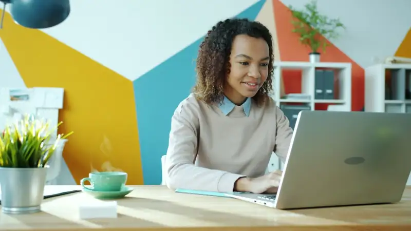 A woman smiling while she works on a laptop at her desk